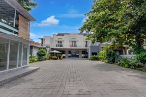 Ein Hotel mit Eingangsbereich, gepflastertem Innenhof, überdachter Sitzgelegenheit und üppiger Bepflanzung.