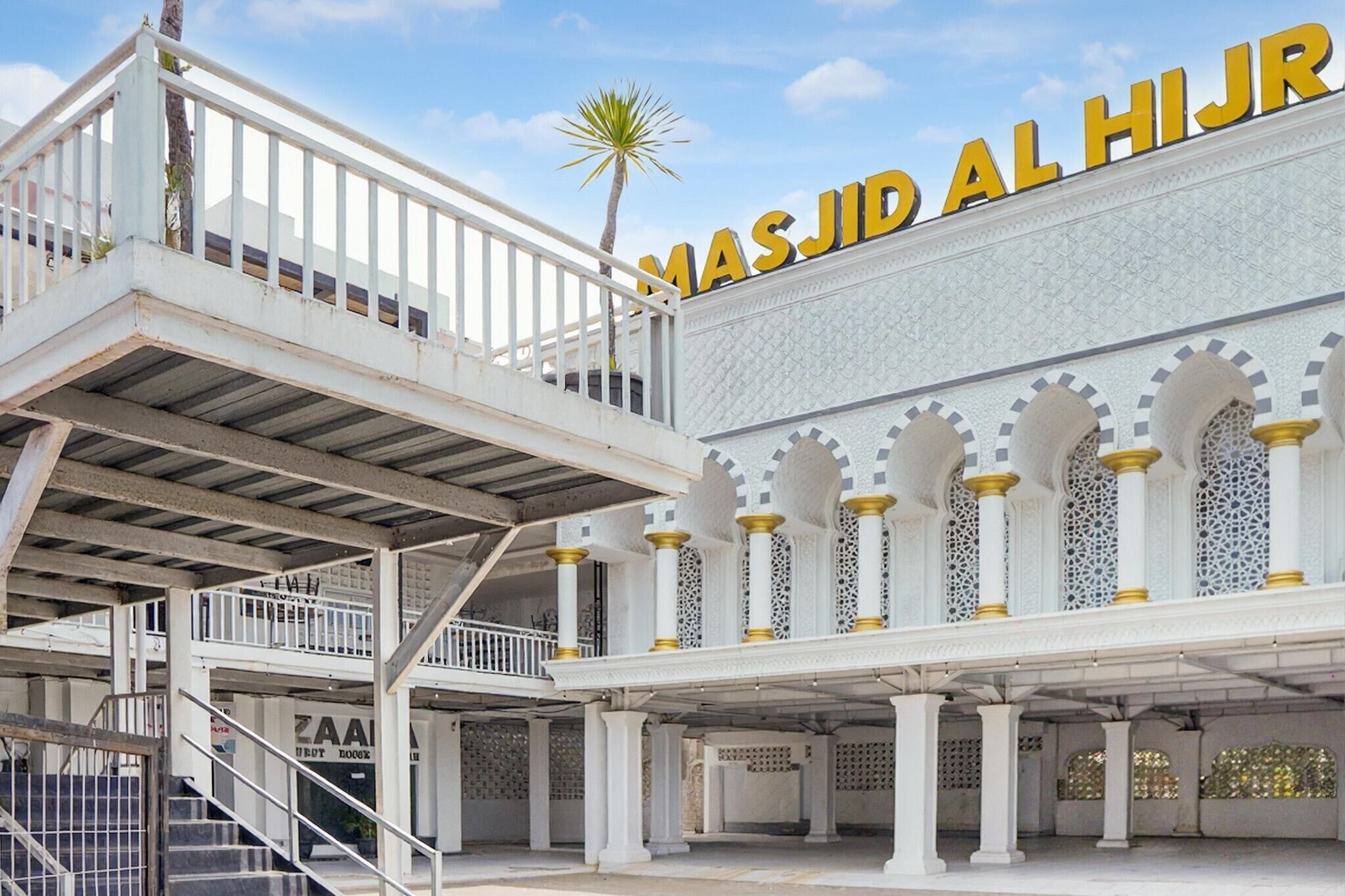 Un edificio de varios niveles con un cartel llamativo que dice 'MASJID AL HIJR' y una escalera que lleva a un nivel superior.