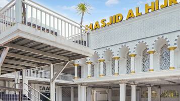 A multi-level building with a prominent sign reading 'MASJID AL HIJR' and a staircase leading to an upper level.