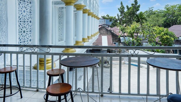 Un balcon orné de colonnes blanches, d’où l’on peut admirer un bâtiment traditionnel aux motifs complexes.