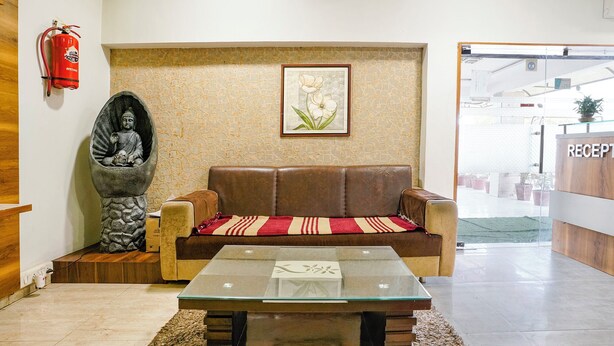Un espace d’accueil comprenant un canapé en cuir marron, une table basse en verre, une œuvre d’art florale encadrée, une statue de Bouddha et un extincteur.