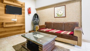 Un salon avec un canapé en cuir marron, une table basse en verre, un téléviseur fixé au mur, un extincteur et une œuvre d’art encadrée accrochée au mur.