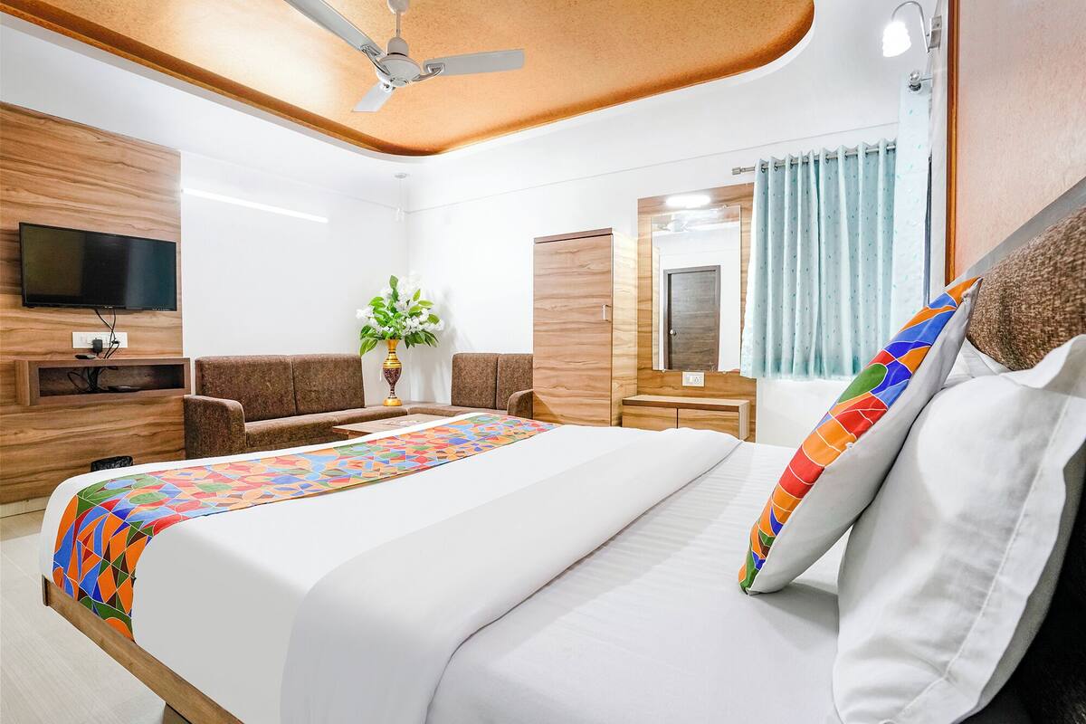 A hotel room with a bed, a TV, a sofa, a desk, and a ceiling fan.