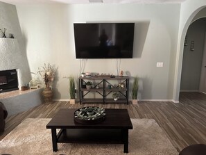 Una sala de estar con televisor de pantalla plana montado en la pared, una mesa de centro de madera oscura y una consola decorativa con plantas.