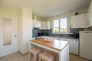 A modern kitchen with white cabinets, a wooden island, and a view of the outdoors. - Holiday Home 'La Maison Et L'étang De Pêche' with Mountain View, Private Terrace and Wi-Fi (Vagney)