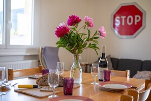 A dining table with a vase of flowers, wine bottle, and glasses. - Holiday Home 'La Maison Et L'étang De Pêche' with Mountain View, Private Terrace and Wi-Fi (Vagney)