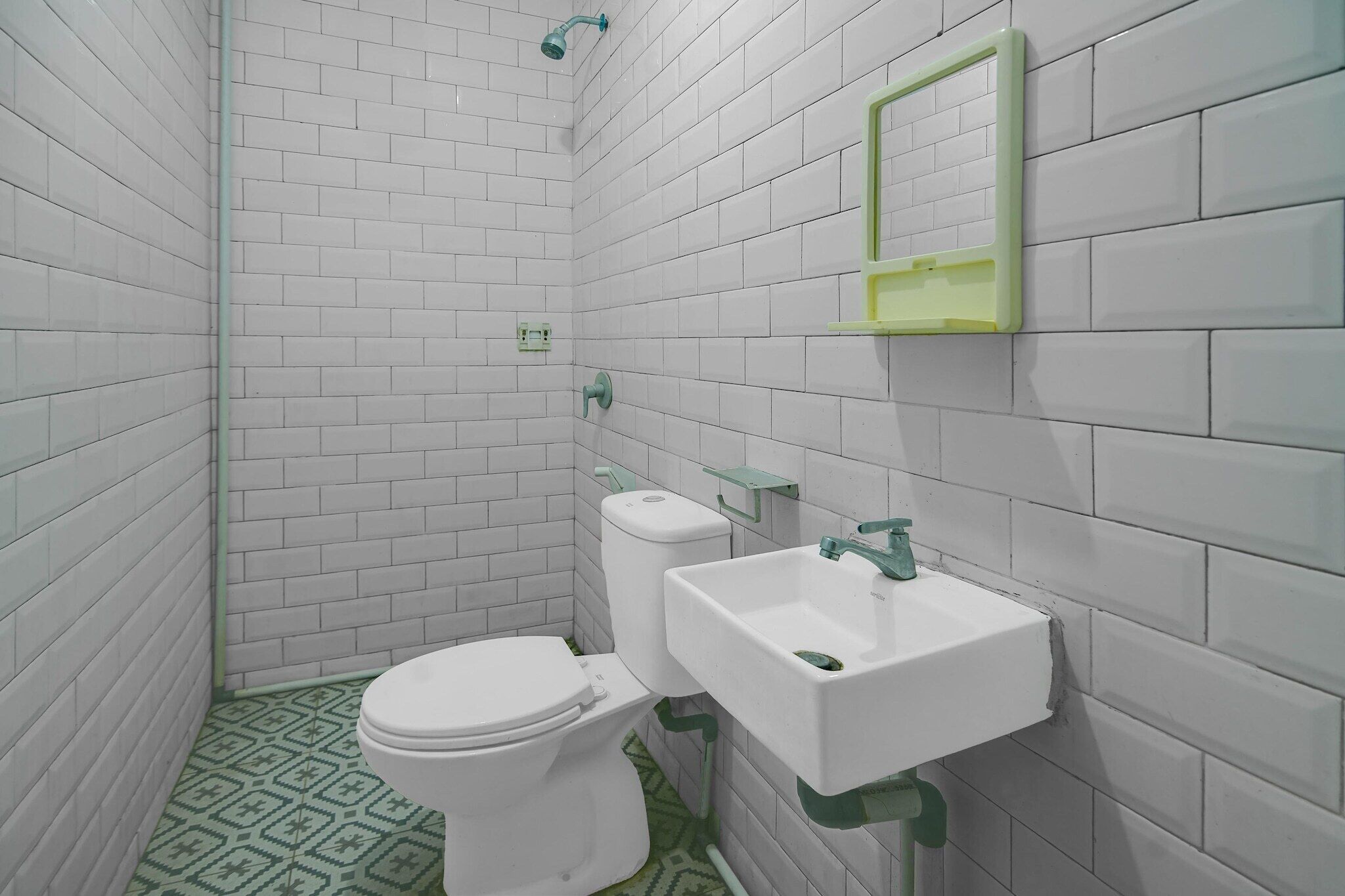 Un baño pequeño con paredes de azulejos blancos, un inodoro blanco, un espejo con marco verde y un lavamanos blanco.
