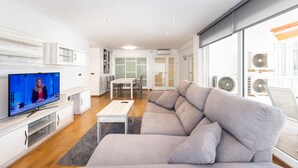 Ein modernes Wohnzimmer mit Fernseher, Sofa, Essbereich und großen Fenstern.