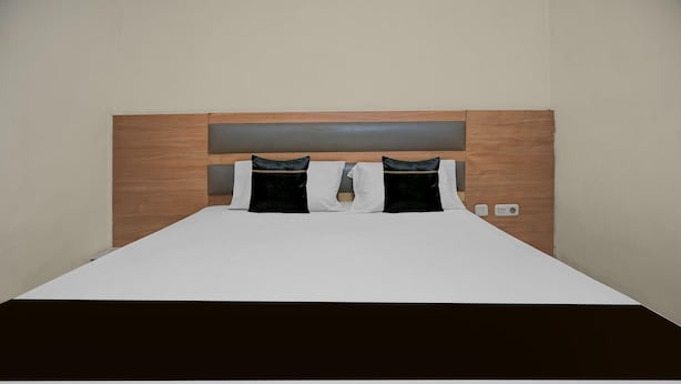 A bed with a wooden headboard, two black and white pillows, and a white bedspread. - Spacious Double Suite Haven w/ Free Parking & WiFi (Makassar)