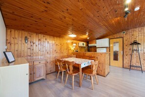 Een houten interieur met een eettafel, stoelen, kasten, een koelkast en een trap.
