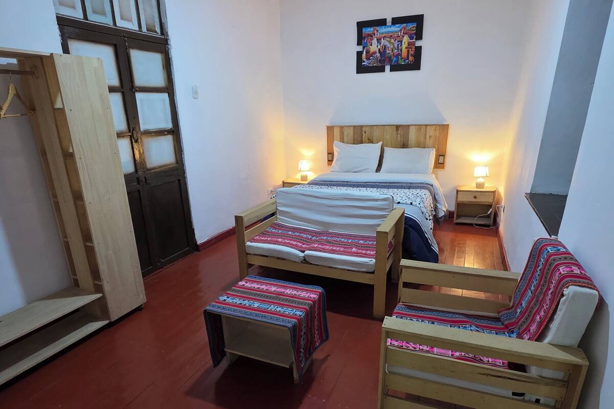 Un dormitorio con una cama de madera, mesitas de noche, un banco y una puerta.
