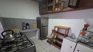 Een keuken met een gasfornuis, een koelkast, een houten plank en een kast met glazen deuren.