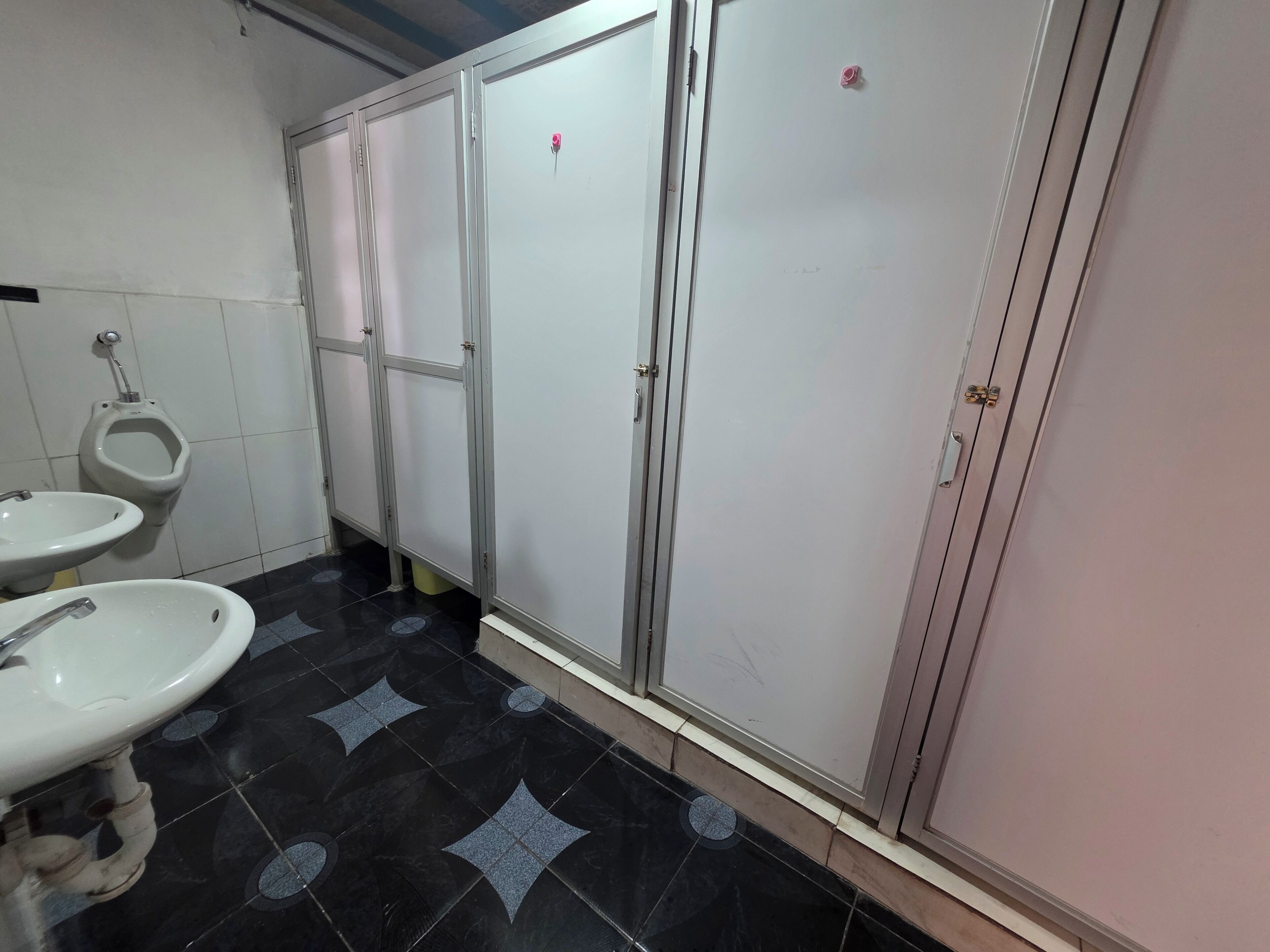 Des toilettes pour hommes avec deux lavabos, un urinoir et des toilettes classiques.