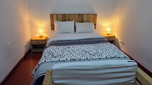 Een net opgemaakt bed met een houten hoofdbord, twee bedlampjes en een ingelijst beeld boven het bed.