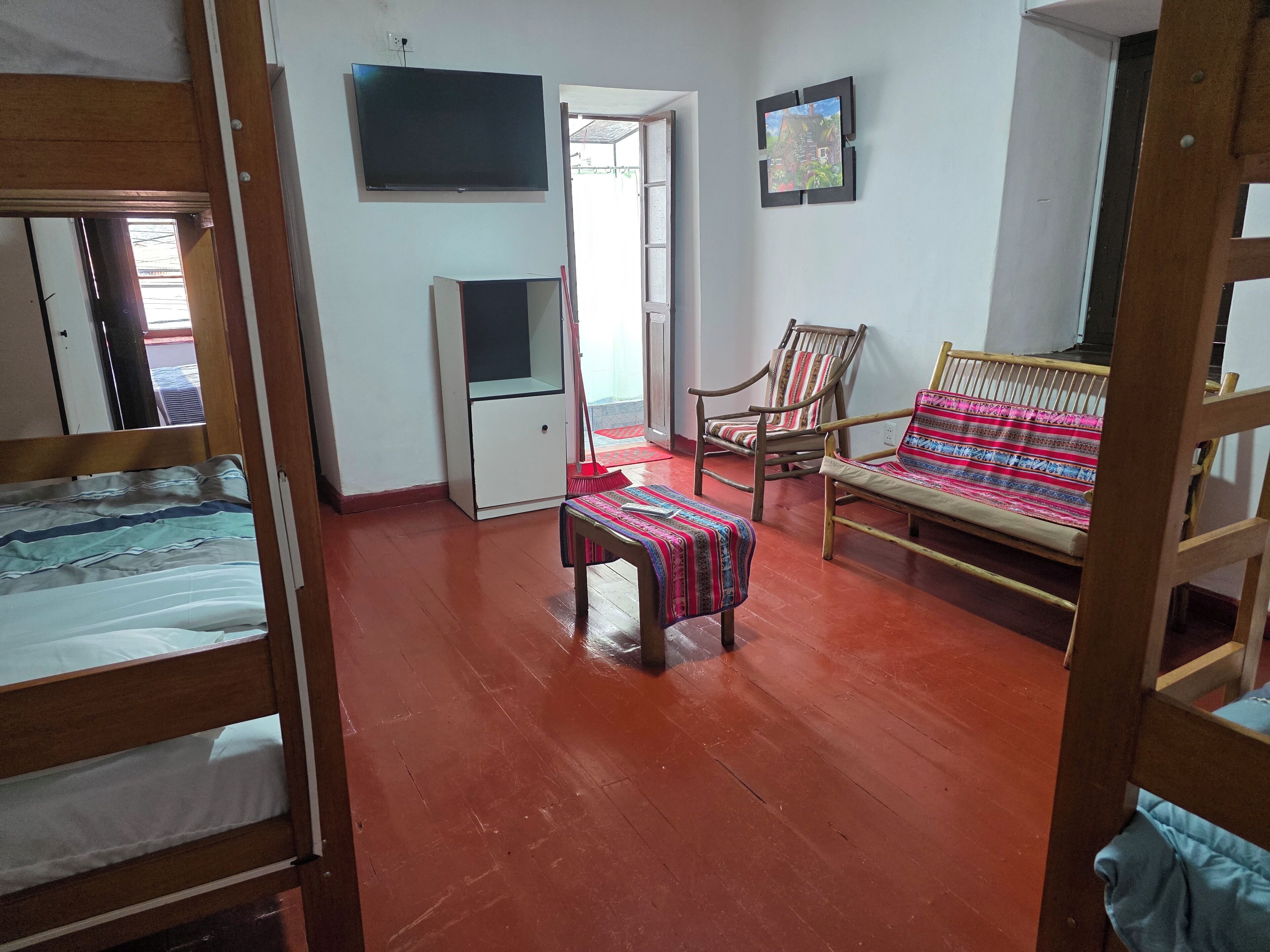 Ein Zimmer mit einem Bett, einem Schreibtisch, einem Stuhl, einem Fernseher und einer Tür, die nach draußen führt.