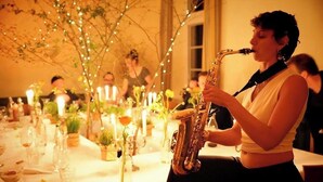 Une personne joue du saxophone à une table décorée de bougies et de fleurs.