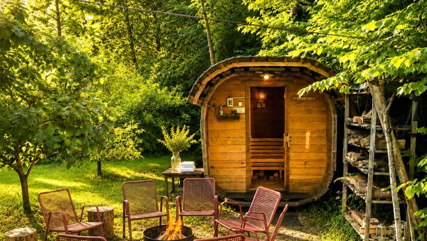 Une cabane en bois avec un foyer et des chaises, située dans un jardin luxuriant.
