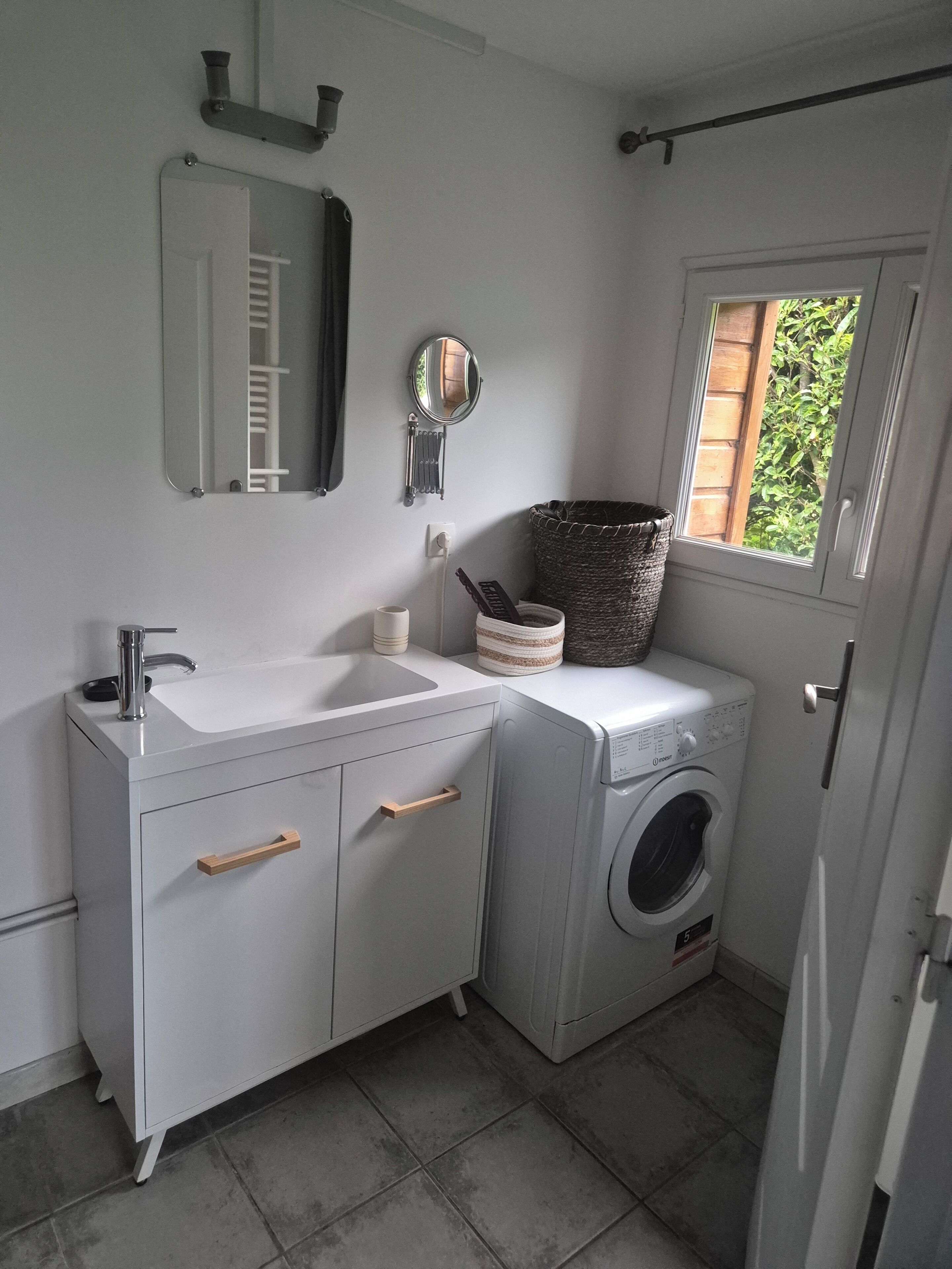 Ein kleines, modernes Badezimmer mit Waschbecken, Spiegel und Waschmaschine in Weiß.