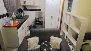 Un espacio habitable compacto con kitchenette, un sofá con almohadas y un pequeño comedor.