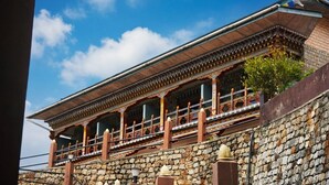 A traditional building with a stone wall, a balcony with railings, and a clear blue sky. - Tendrel Resort (Trongsa)