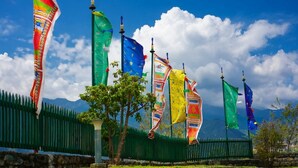 A row of flags on a fence with a clear blue sky and mountains in the background. - Tendrel Resort (Trongsa)