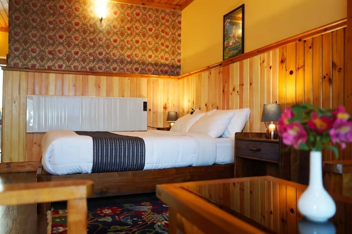Una habitación con paneles de madera, una cama, mesitas de noche, una lámpara y un jarrón con flores.