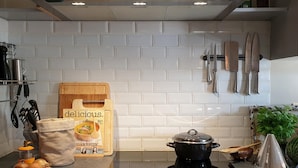 A kitchen with white tiles, a black stove, a wooden cutting board, a bag of flour, and hanging knives. - Villa with swimming pool near Durbuy (Barvaux)