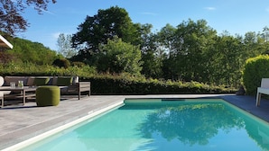 A rectangular swimming pool with a tiled deck, surrounded by greenery and trees. - Villa with swimming pool near Durbuy (Barvaux)