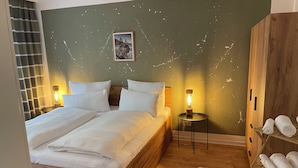 Ein Schlafzimmer mit einem hölzernen Bett, zwei Nachttischlampen, einem Nachttisch, einem Holzschrank und einem Regal mit aufgerollten Handtüchern.