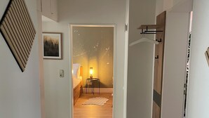 Ein Flur mit Holzboden, einem gerahmten Bild an der Wand, einem kleinen Tisch mit Lampe und einem Kleiderständer.