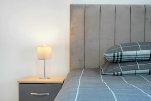 A bed with a headboard, a bedside lamp, and a drawer unit. - Bright and Inviting 1BDR Flat in Kentish Town (Greater London)
