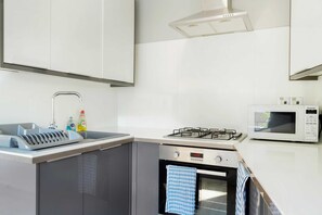 Une cuisine équipée d’un four encastré, d’un four à micro-ondes, d’une cuisinière à gaz et d’un évier avec un égouttoir à vaisselle.