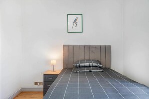 Une chambre à coucher avec un lit, une table de chevet, une lampe, un tableau encadré au mur et un plancher en bois.