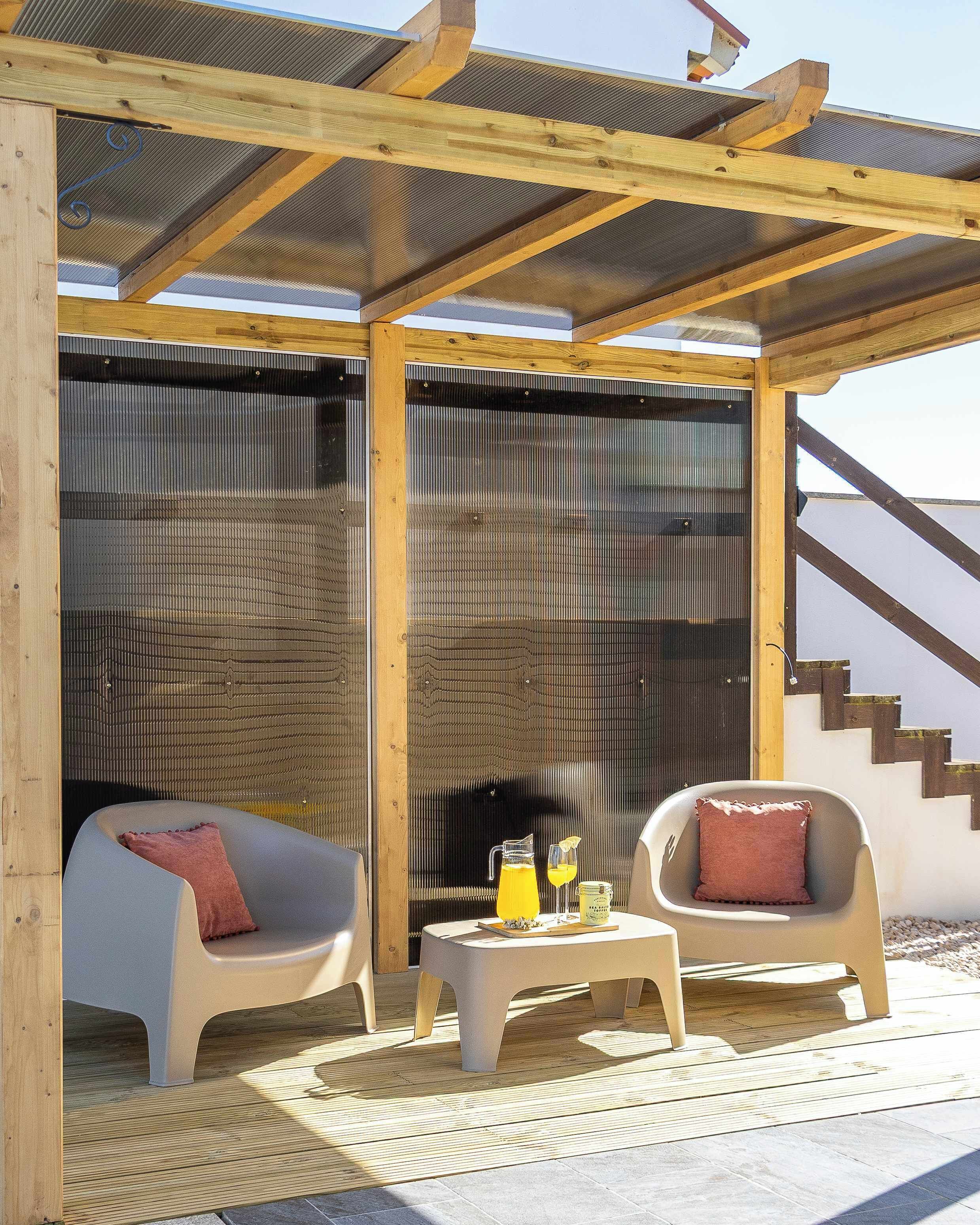 A covered outdoor seating area with two chairs, a small table, and a beverage.