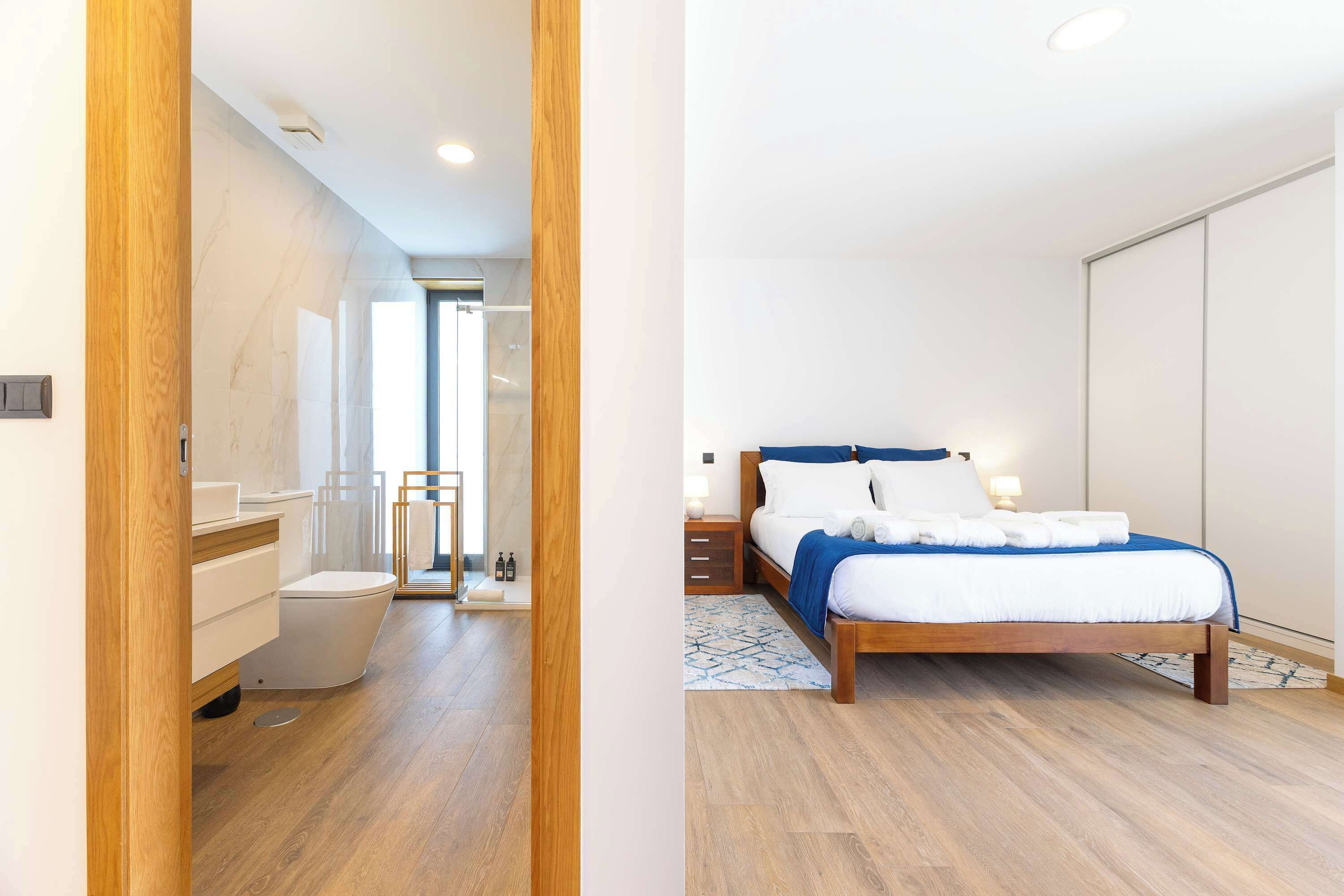 Une chambre à coucher moderne avec un lit en bois, une literie blanche et une table de chevet avec une lampe.