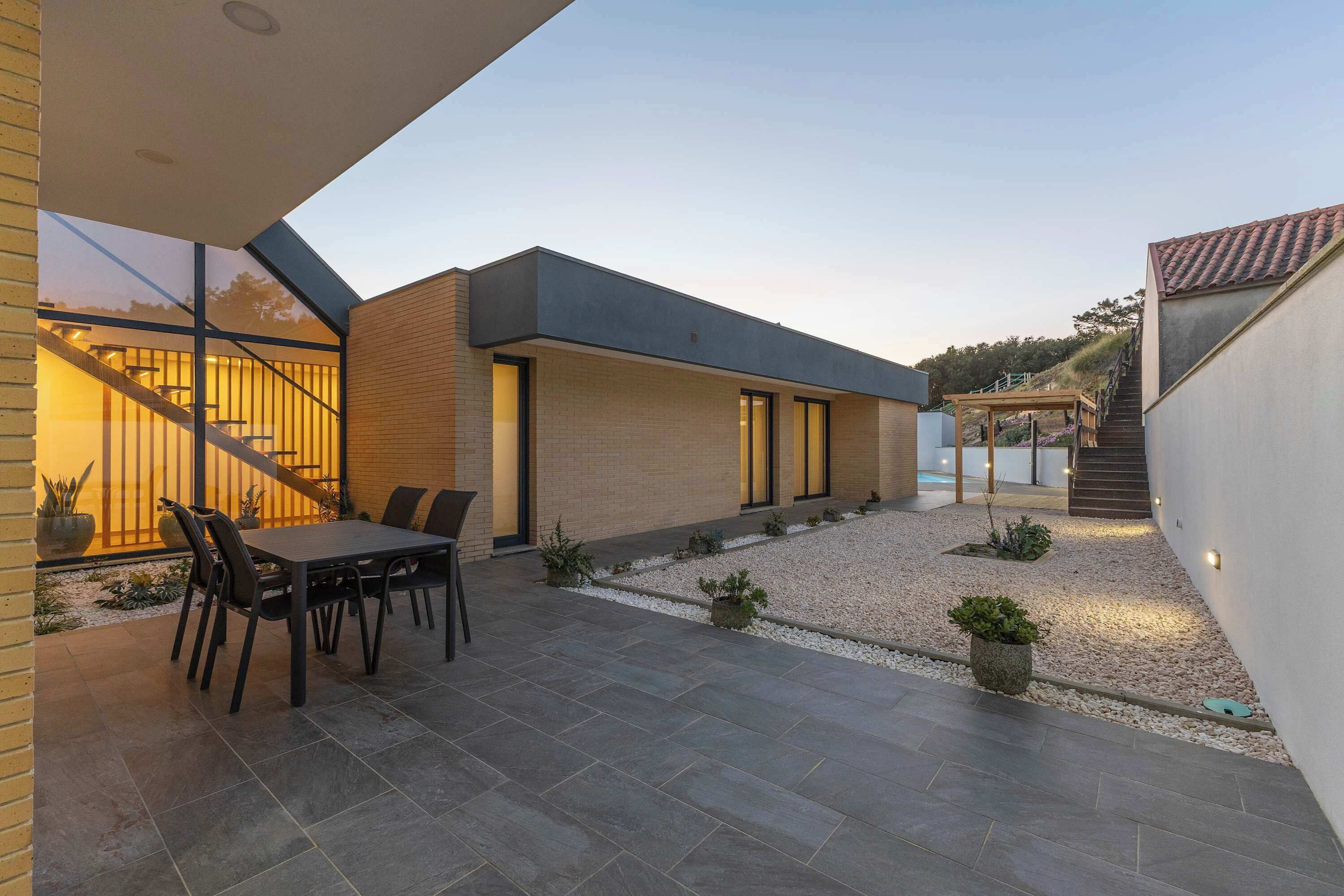 Una casa moderna con patio, mobiliario exterior y una escalera que lleva a un espacio cubierto.