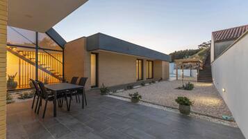 Una casa moderna con patio, mobiliario exterior y una escalera que lleva a un espacio cubierto.
