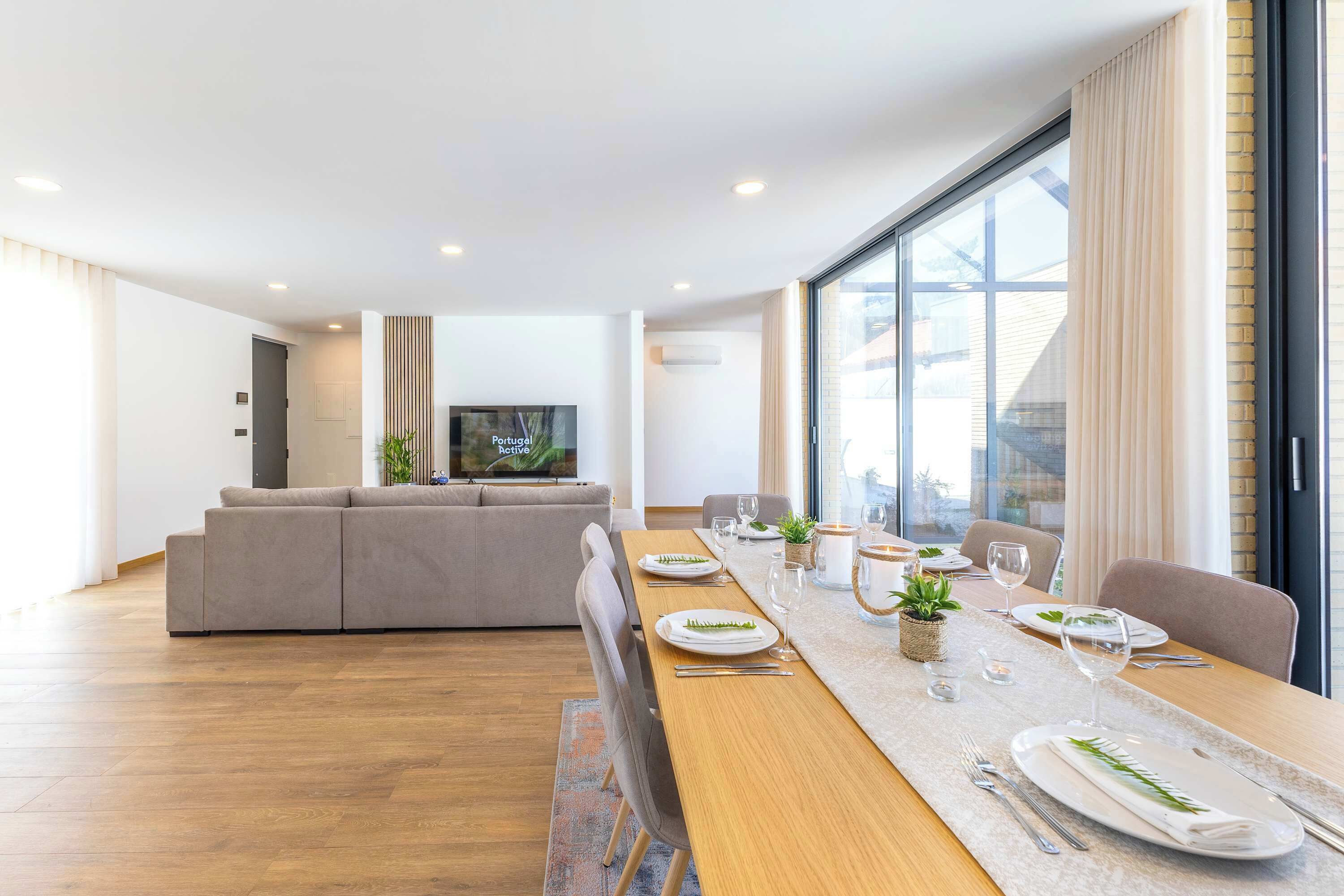 Una sala de estar moderna con un sofá, una mesa de comedor con platos y vasos, y un televisor en la pared.
