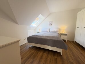 A bedroom with a skylight, a bed with a grey blanket, a bedside table with a lamp, and a wardrobe.