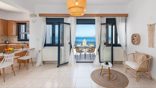 A modern kitchen with white cabinets and a dining area with a view of the sea. - Sacada Seascape Villa (Nisiros)