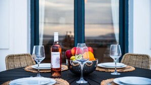 A dining table with a bottle of Corali wine, a bowl of fruit, and empty wine glasses. - Sacada Seascape Villa (Nisiros)