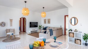 A modern living room with a sofa, TV, and dining area with a fruit bowl and blue glassware. - Sacada Seascape Villa (Nisiros)