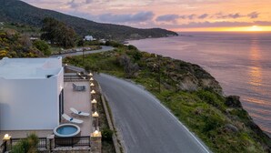 A coastal road with a pool area, lounge chairs, and a sunset view. - Sacada Seascape Villa (Nisiros)