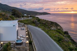 A coastal road with a pool area, lounge chairs, and a sunset view.