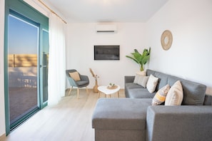 A modern living room with a grey sofa, a small coffee table, a chair, and a potted plant. - Gemini Villas - Horizon (Rhodes)