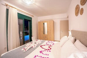 A hotel room with a bed, a wooden wardrobe, a green door, and a bathroom visible through a glass door. - Gemini Villas - Horizon (Rhodes)