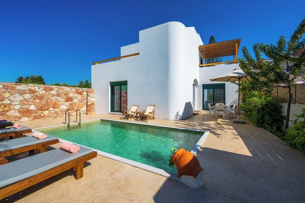 Eine moderne Villa mit Swimmingpool, Liegestühlen und einer Steinmauer.