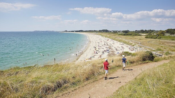 A beach with a dirt path leading to the water, populated with people.