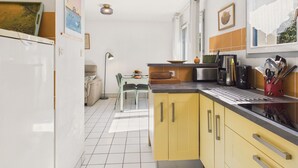 A compact kitchen with yellow cabinets, a black countertop, and a dining area with a table and chairs.