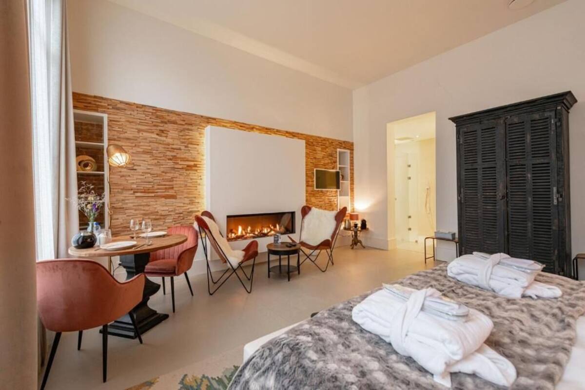 A modern hotel room with a fireplace, a dining area, and a bed with towels.